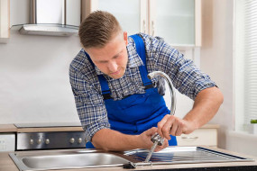Tradesman installing new tap over stainless steel sink